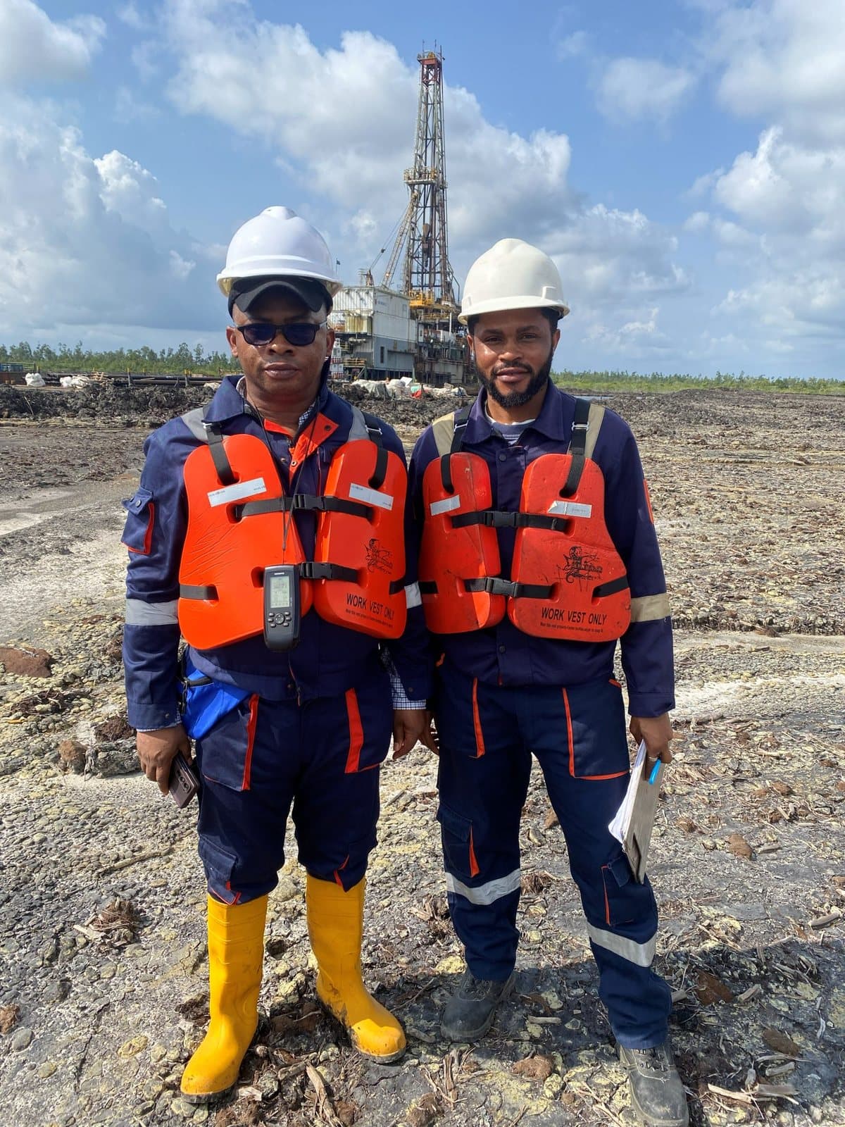 Joseph Legend Mfon on a Niger Delta site survey, in field kit beside a drilling rig.
