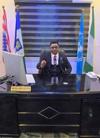 Joseph Legend Mfon at his desk beneath the flags of the United States, the United Nations and Nigeria.